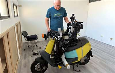 Prof. Hansjörg „Jacky“ Baltes neben einem humanoiden Roboter, der einen Scooter fährt. Das Projekt dient als Forschungsplattform für Balance, Steuerung und Wahrnehmung in der Robotik. (Foto: Alexander Kunz)