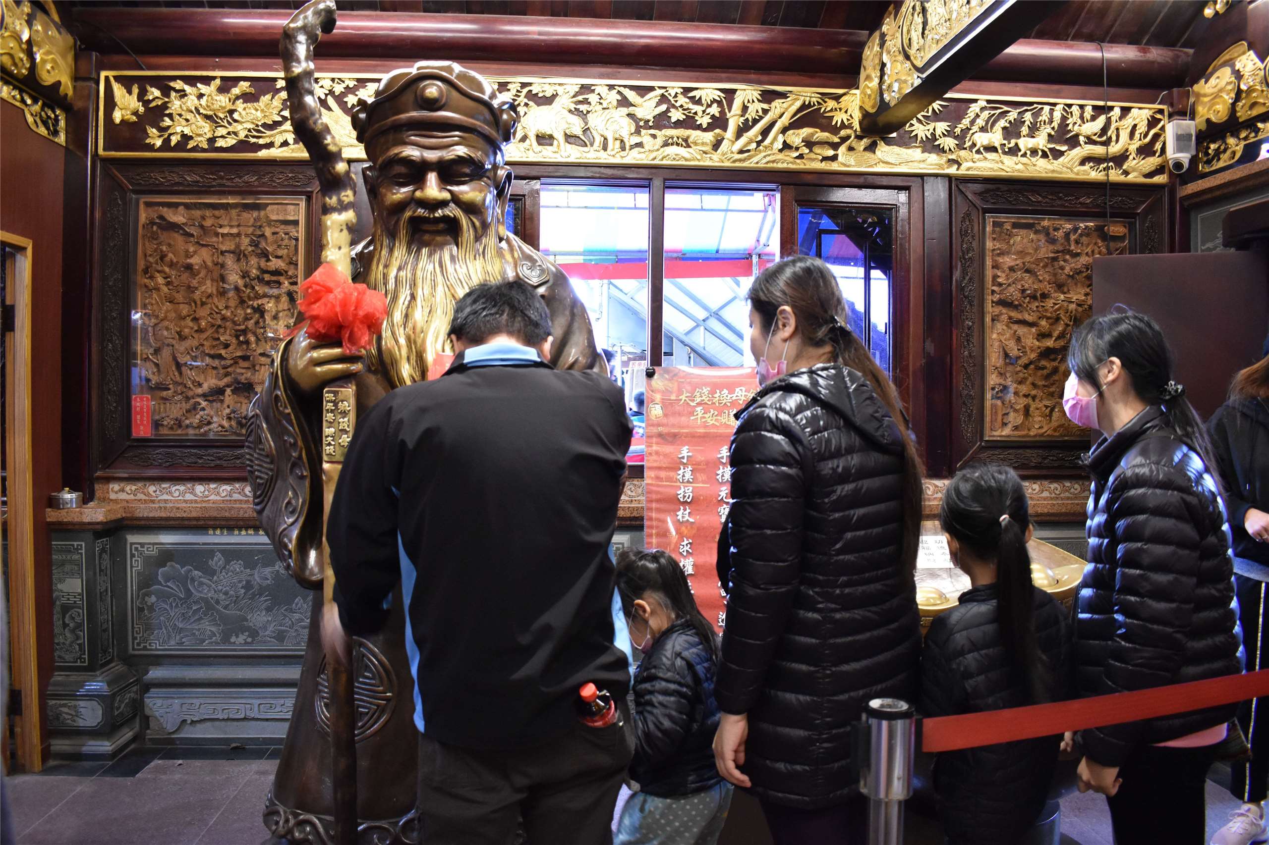 La statue de bronze de Tudi Gong dans la salle principale. On insère dans le lingot une pièce de 10 NTD afin de récupérer, dans la manche, une pièce de 1 NTD, considérée comme « monnaie source de richesse » (qianmu 錢母). Une affiche invite les pratiquants à toucher le lingot d’or pour obtenir de la richesse (caifu 財富), la barbe pour souhaiter du bonheur (fuqi 福氣) et de la progéniture (shengzi 生子), et le bâton pour obtenir prospérité et une bonne position dans la société (fugui 富貴) (photo Marta Pavone, aimable crédit)