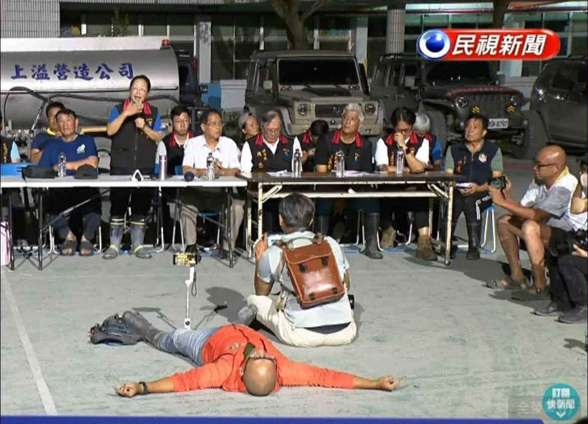 花蓮縣長徐榛蔚在部落族人要求下對救災工作進行說明時，佐拉(穿著橘色外套者)對縣長的冗長發言不耐，直接在地上躺平表達抗議。(網路截圖)