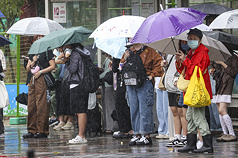 圖為民眾撐傘在雨中等公車。資料照。