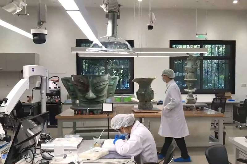 圖為中國三星堆文物保護與修復館，桌上器物從左至右為青銅大面具、青銅尊與頂尊跪坐人像。(翻攝維基百科)