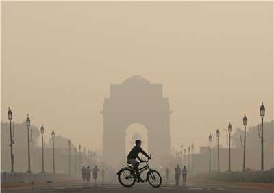 圖為戴著口罩的1名男子在空污嚴重的上午，騎自行車經過位於印度首都新德里的印度門。 (檔案照)
