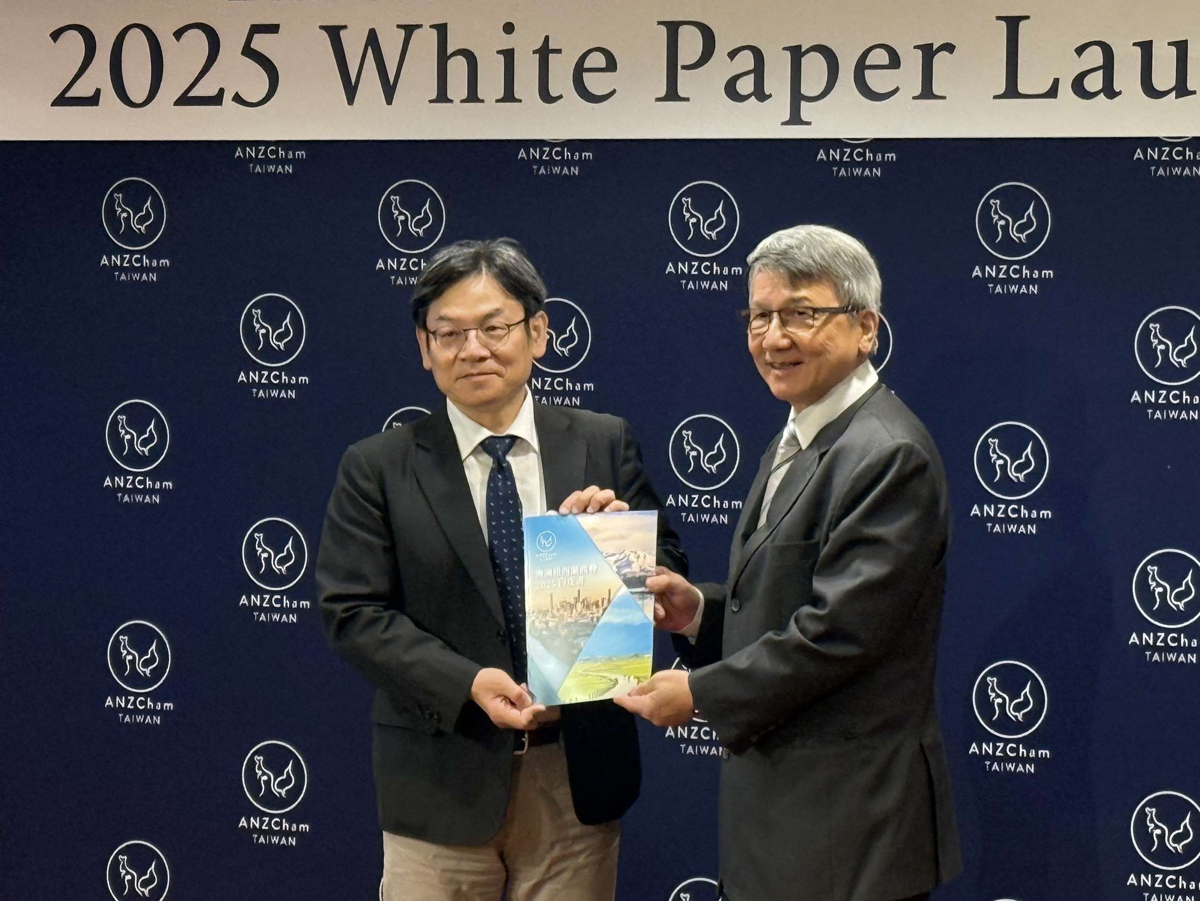 國發會主委葉俊顯(左)自澳紐商會理事長陳明信(右)手中接下今年澳紐商會白皮書。(謝佳興 攝)