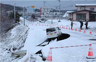受到青森縣強震影響，當地一輛汽車卡在斷裂的雪地馬路坑洞。