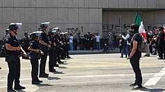 洛杉磯數百人群眾聚集在聯邦政府大樓前，抗議移民
暨海關執法局（ICE）突襲掃蕩非法移民，一名示威
者手拿墨西哥國旗，在一排警察面前站立表示抗議。
