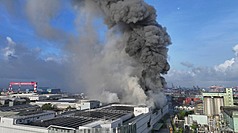 高雄市小港區三元能源公司建築14日清晨5時許發生火警，現場建築冒出大量濃煙，經消防員布水線灌
救，火勢持續控制中。（高雄市政府消防局提供）