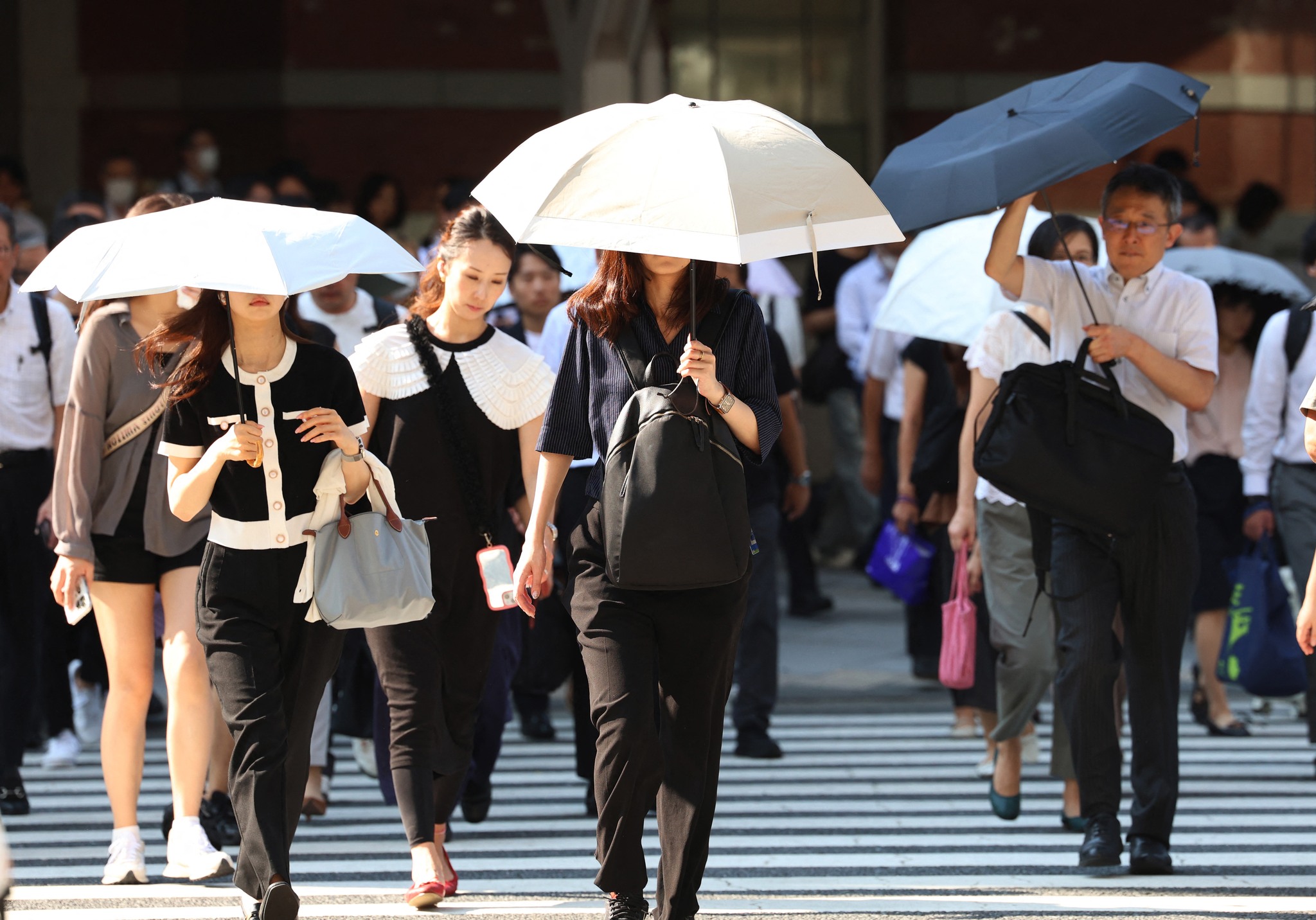 東京連日高溫，通勤族忙撐傘遮陽。