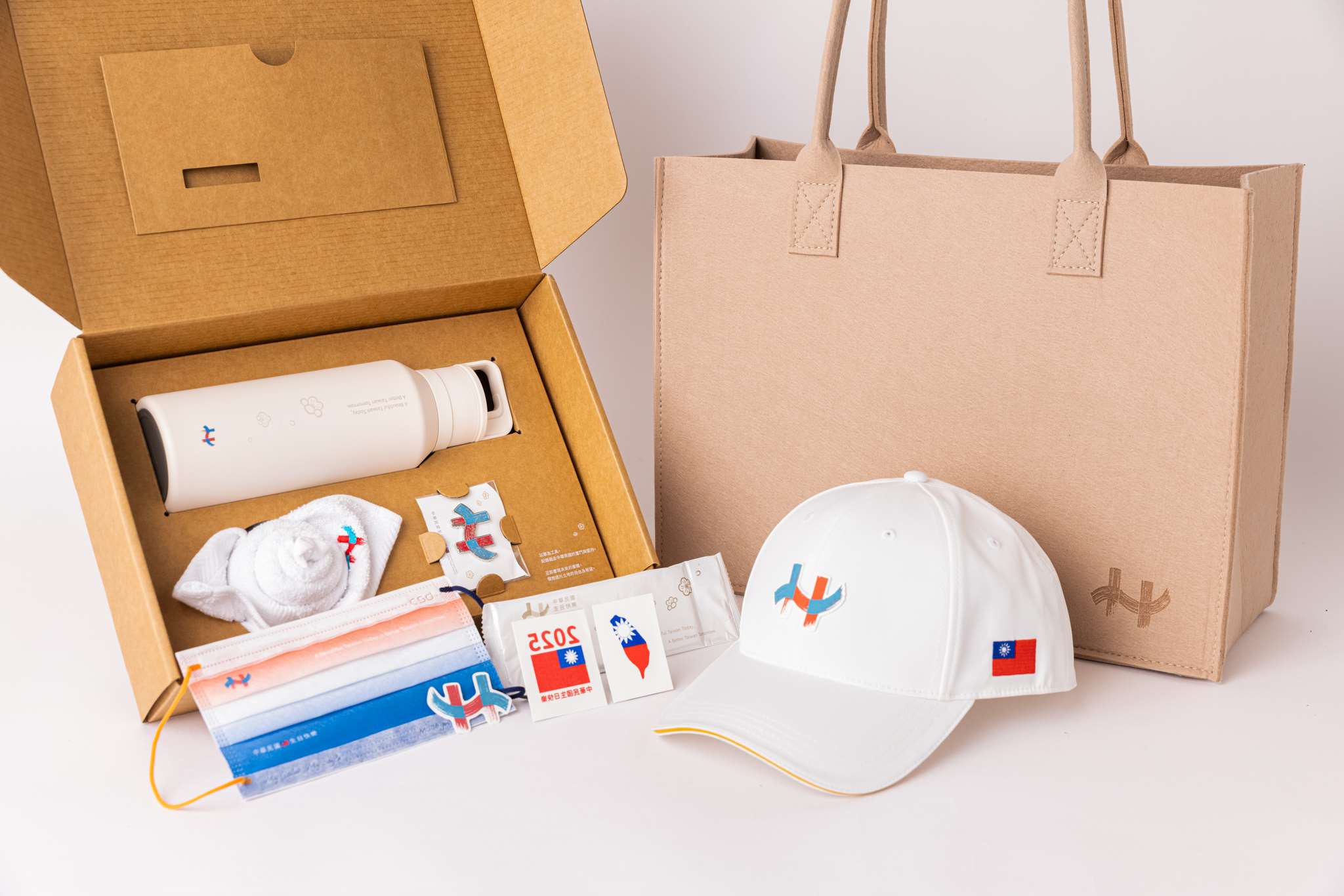 國慶籌備委員會18日展示114年國慶禮賓紀念品，除 了棒球帽外，首創以禮盒將徽章、保溫瓶、方巾及口 罩搭配呈現，還特別將毛巾摺成玫瑰花。(圖：慶籌會提供)