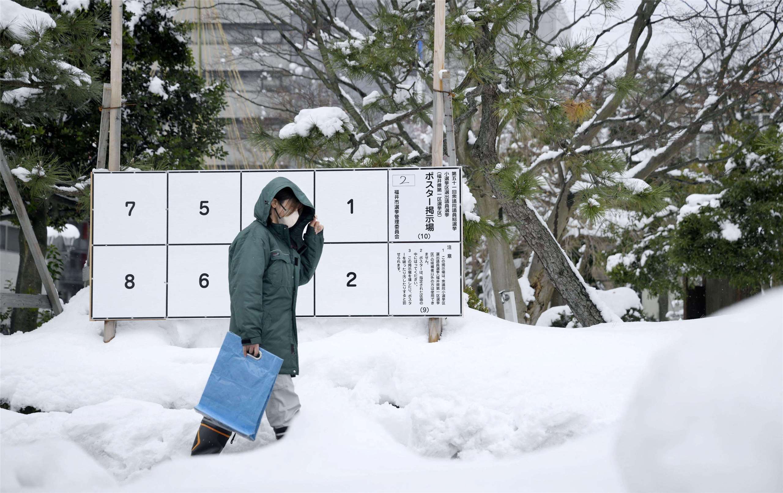 日本首次在嚴冬中舉行眾院改選，一名行人走在積雪道路上經過一塊張貼2月8日提前選舉候選人海報看板。(路透社/達志影像)
