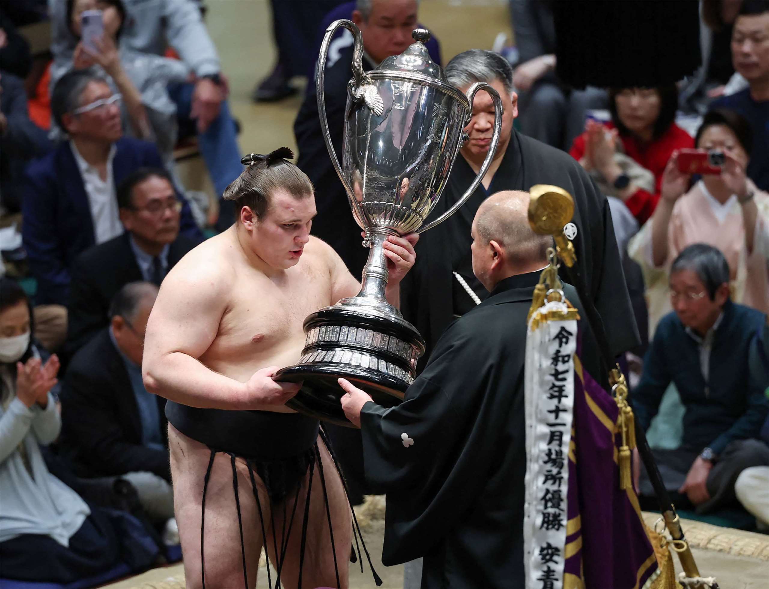 烏克蘭相撲選手安青錦(Danylo Yavhusishyn)在東京國技館舉行的1月大相撲錦標賽中奪冠後領取獎盃(圖)，而「內閣總理大臣盃」則改由文部科學大臣松本洋平代為登上土俵。(AFP)