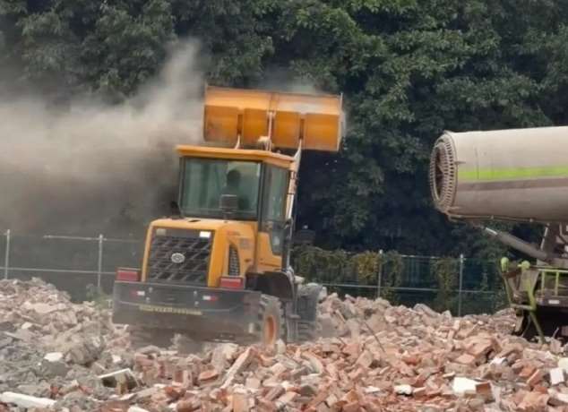 一台鏟車將泥土磚瓦高舉，對準一部大型霧炮機，瞬間揚起漫天塵土。(翻攝微博)