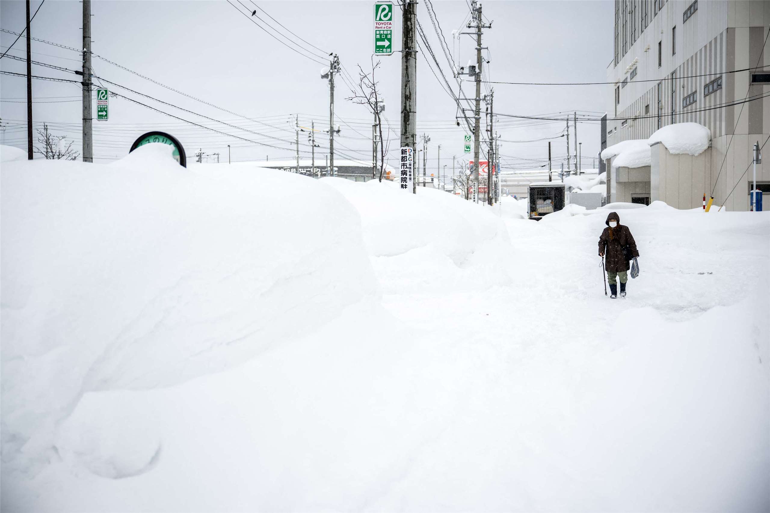 受到強烈寒流壟罩影響，日本的日本海側地區連日大雪，青森縣青森市積雪更高達1.8公尺，創下40年來新高。圖為青森市民走在比人高的雪堆旁。(AFP)