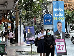 泰國曼谷街道掛有各黨總理及眾議員候選人看板。圖為民眾在選舉看板旁的公車站等車。