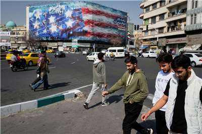 2月22日攝於伊朗德黑蘭的伊斯蘭革命廣場，行人走過一幅廣告看板。看板上描繪著一艘美國航空母艦，甲板上停放著受損的戰鬥機，並以波斯語和英語寫著標語：「種下風暴，必將收穫旋風」。