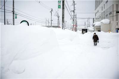 受到強烈寒流壟罩影響，日本的日本海側地區連日大雪，青森縣青森市積雪更高達1.8公尺，創下40年來新高。圖為青森市民走在比人高的雪堆旁。(AFP)