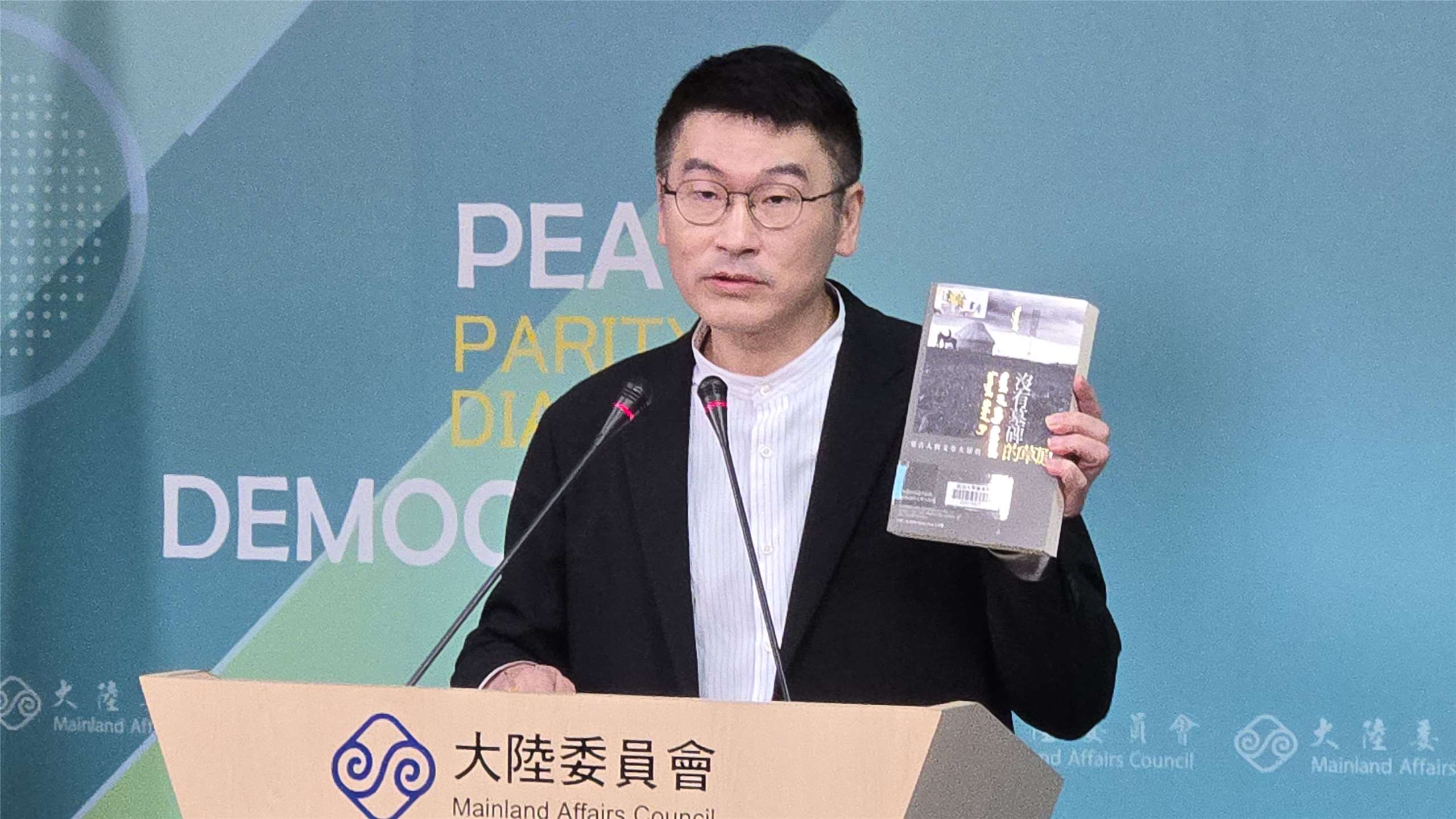 陸委會副主委梁文傑在記者會上，拿出八旗文化總編輯富察出版的書。(陳國維 攝)