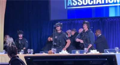 白宮記者晚宴會場傳出槍響後，荷槍實彈的特勤人員奔上舞台保護川普(中後方)。(X平台/@BoKnowsNews)