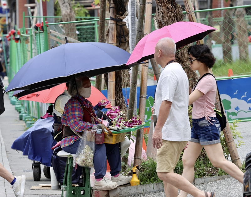 中央氣象署21日下午發布15縣市亮高溫燈號，其中雙北已出現逾38度高溫。圖為台北市萬華區民眾撐傘防曬。
