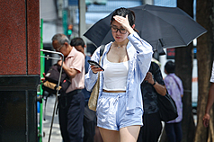 天氣高溫炎熱，新北市板橋區外出民眾以手遮擋刺眼陽光。資料照片。