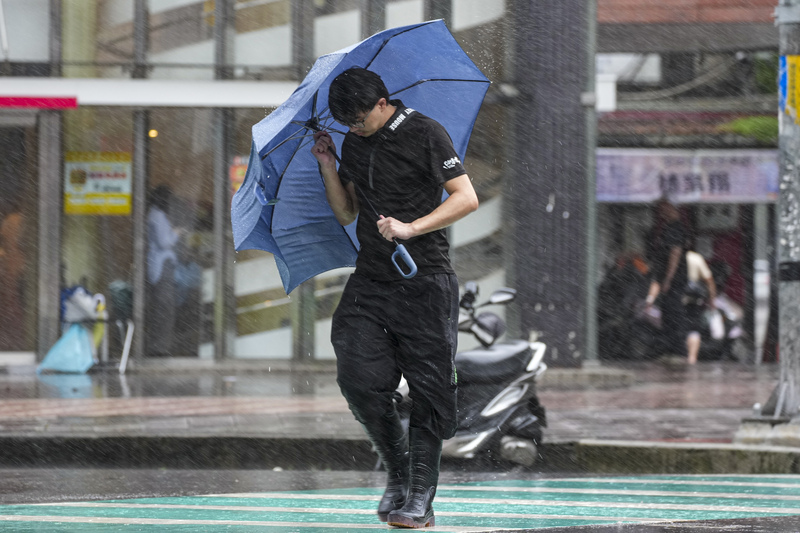 颱風巴威持續減弱、縮小，最快今天(12日)清晨將解除颱風警報。圖為颱風巴威侵襲期間，新北市新店區民眾緊握遭強風吹折的雨傘，快步通過路口。資料照片