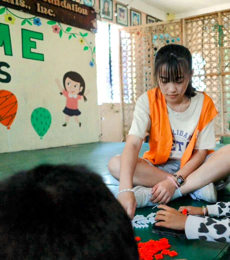 邱琬寧在菲律賓兒少社福機構內指導孩童玩桌遊，在遊戲交流中培養孩童們的邏輯思考。(圖：聖約翰科大提供)