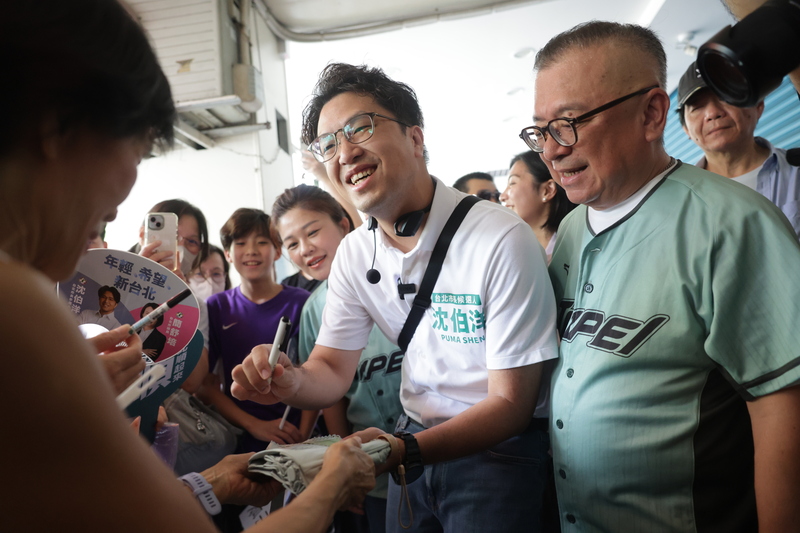 民進黨台北市長參選人沈伯洋（中）13日上午赴東門市場掃街，許多民眾在市場外等候，拿出物品請沈伯洋簽名留念。