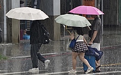 14日、15日西南風增強，中南部不定時有局部大雨發生，15日雨勢最劇。圖為高雄市三民區午後大雨，民眾撐傘前行。