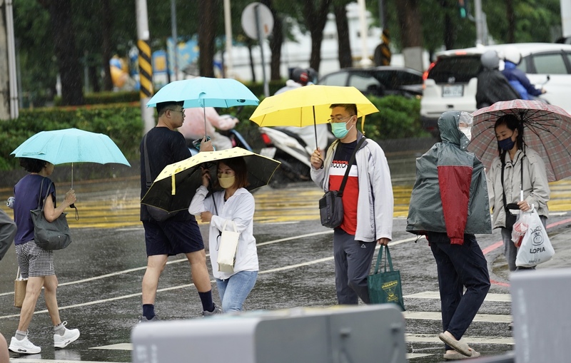 高雄天氣不穩定，民眾穿外套、撐傘過馬路。資料照片。