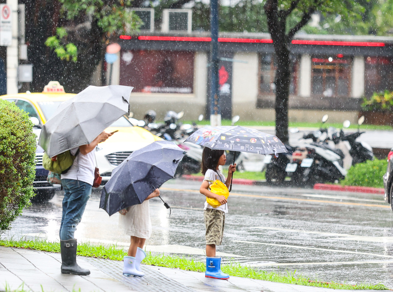 受到颱風外圍雲系影響，今天桃園以北降雨較為明顯，大台北地區及基隆北海岸並有大雨發生的機會，其他地區主要以午後降雨為主。圖為北市中正區街頭民眾撐傘準備過馬路。