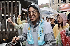 民進黨台北市長參選人沈伯洋（前）6日冒雨前往南京公寓市場拜票，儘管雨勢不小，仍面帶笑容向民眾致意。