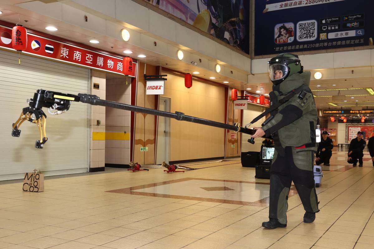 台北市政府與交通部為確保台北車站特定區面對突發危安事件的緊急應變能力，22日下午進行「無差別攻擊事件」聯合危安實兵演練。依規劃，第三階段模擬有名攜帶爆裂物的歹徒逃竄到地下街，遭警方以優勢警力壓制與逮捕，防爆人員全副武裝排除爆裂物。(台北市政府提供)
