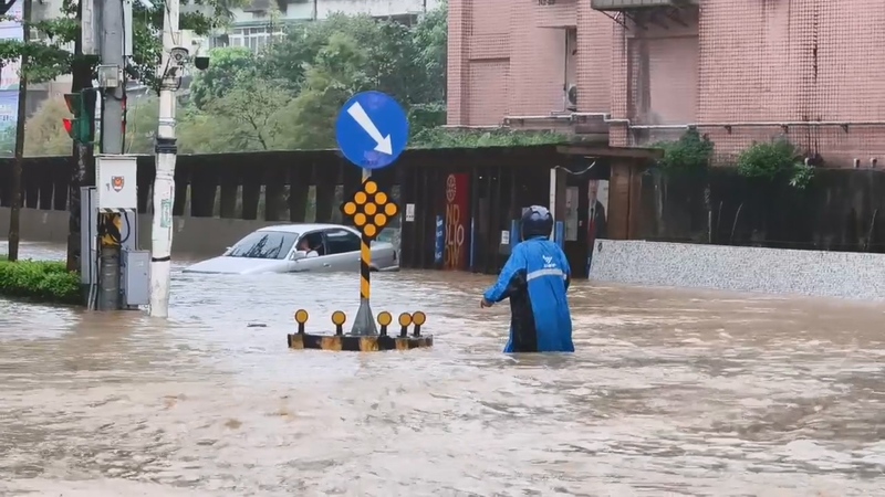 基隆市4日上午強降雨，導致大武崙溪溢流至基金一路沿線。一輛轎車冒險涉水卻拋錨，新崙里長林金龍（藍色雨衣）見狀上前協助，將年長駕駛攙扶至路旁。
（新崙里長林金龍提供）
